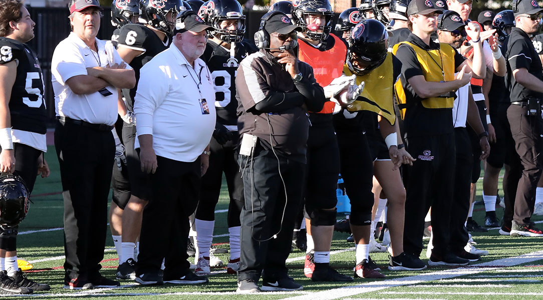Bob Owens stands in front of the team on the sidelines.