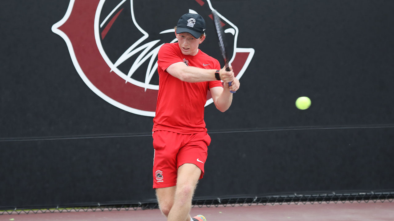 Caleb Wilkins playing tennis, hitting a back hand.