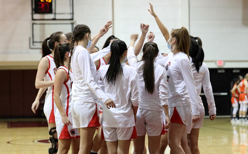 The women's basketball team huddles together on the court.