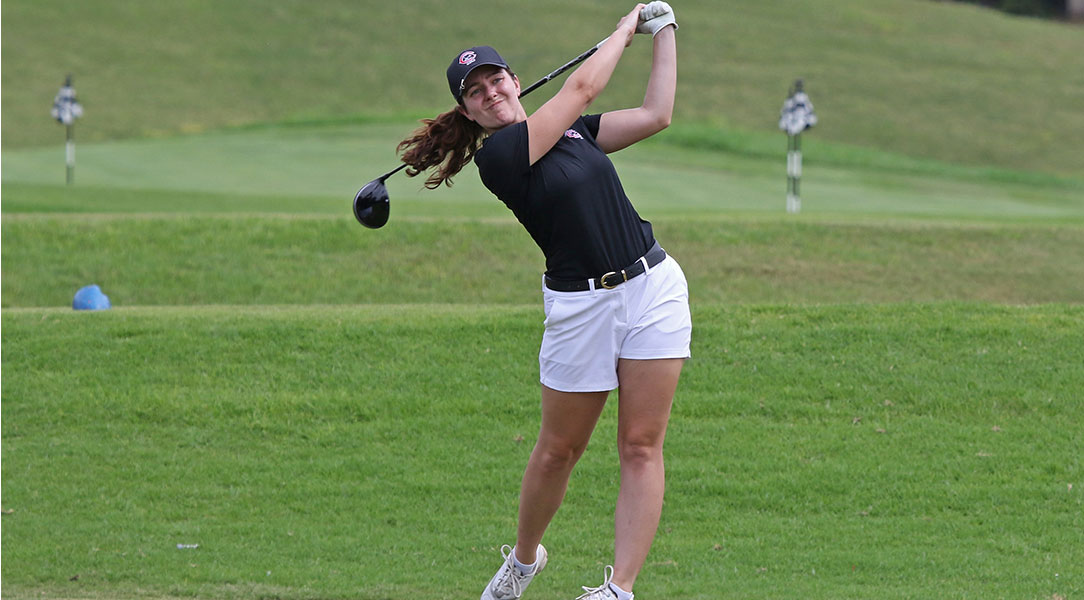 A women's golfer tees off.