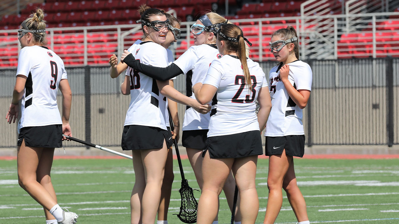 Several lacrosse players huddle together after scoring a goal.