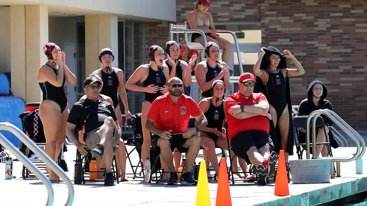 The women's water polo team watches from the bench.